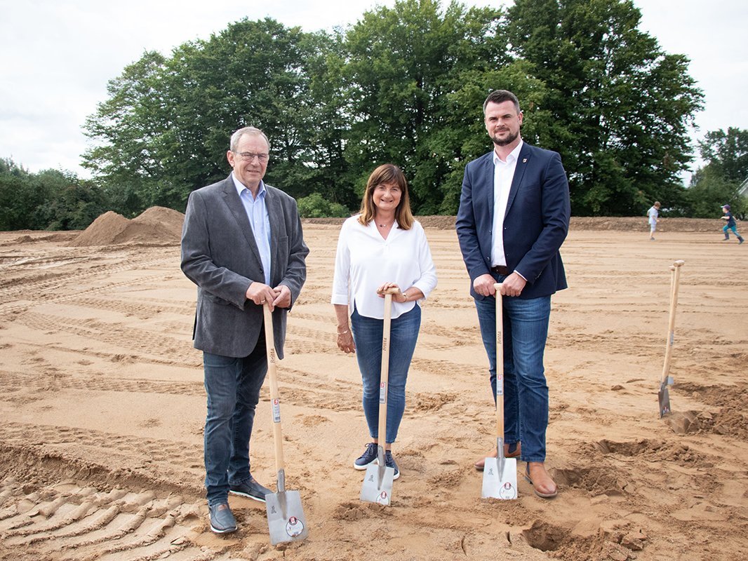 Drei Personen stehen mit Spaten auf einer Baustelle.